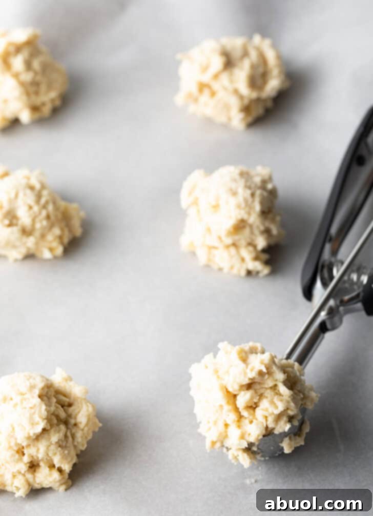 Using a metal cookie scoop to portion biscuit dough onto a baking sheet.