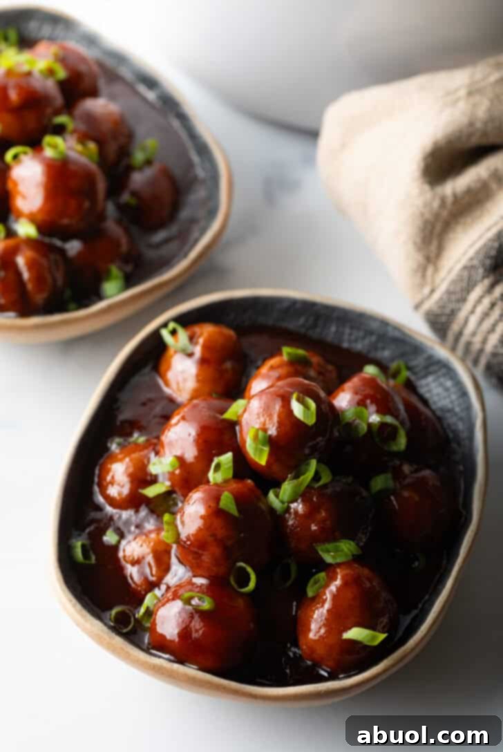 Bowl full of meatballs covered in barbecue sauce, topped with fresh chopped scallions.