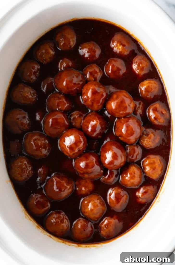 White slow cooker filled with meatballs in bbq sauce.