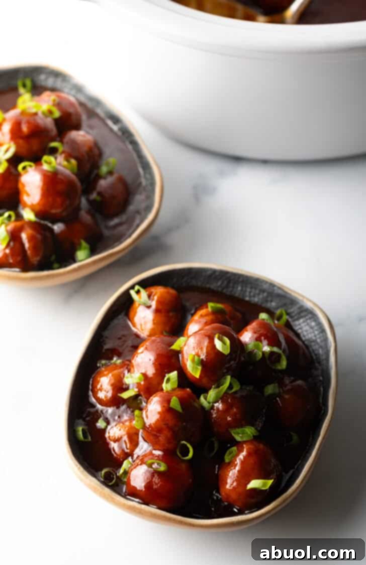 Bowl full of meatballs covered in barbecue sauce, topped with fresh chopped scallions.