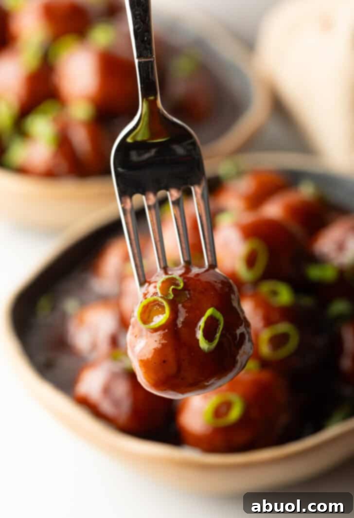 A fork is holding a bbq sauce-coated meatball to camera.