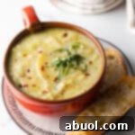 Red oversized mug filled with leek and potato soup, on a plate with slice of baguette on the side.