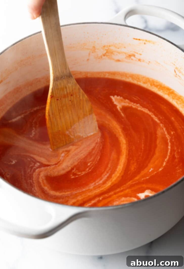 A wooden spatula gently stirring a simmering pot of creamy tomato soup, creating swirls of vibrant red and white.