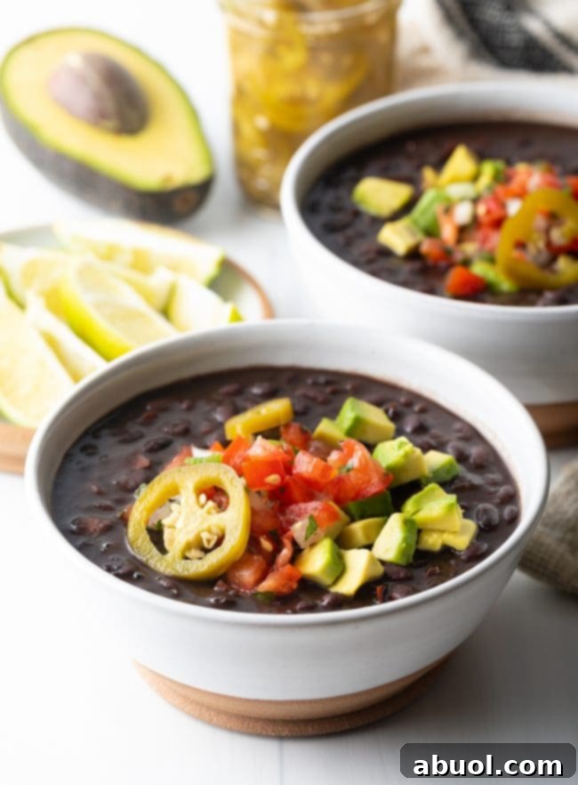 Two white bowls of black bean soup topped with slices of jalapenos, chopped avocado, and pico de gallo.