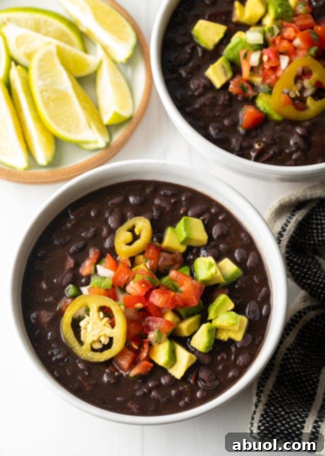 Top down two white bowls of black bean soup topped with slices of jalapenos, chopped avocado, and pico de gallo.