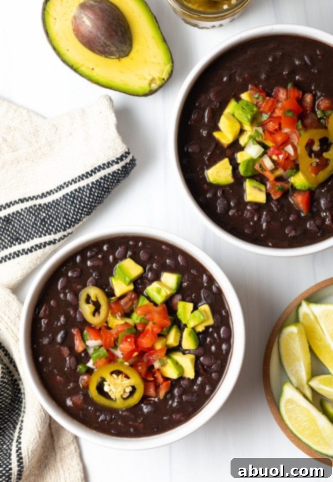 Easy Black Bean Soup - Top down two white bowls of black bean soup topped with slices of jalapenos, chopped avocado, and pico de gallo.