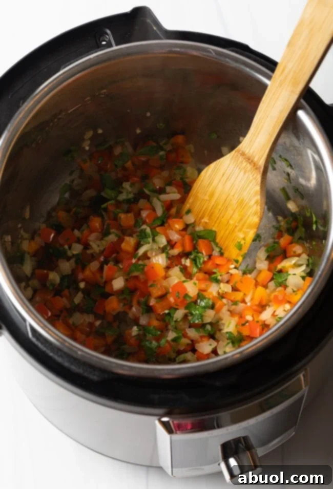 Sauteed red peppers and onions in an instant pot with a wooden spatula.
