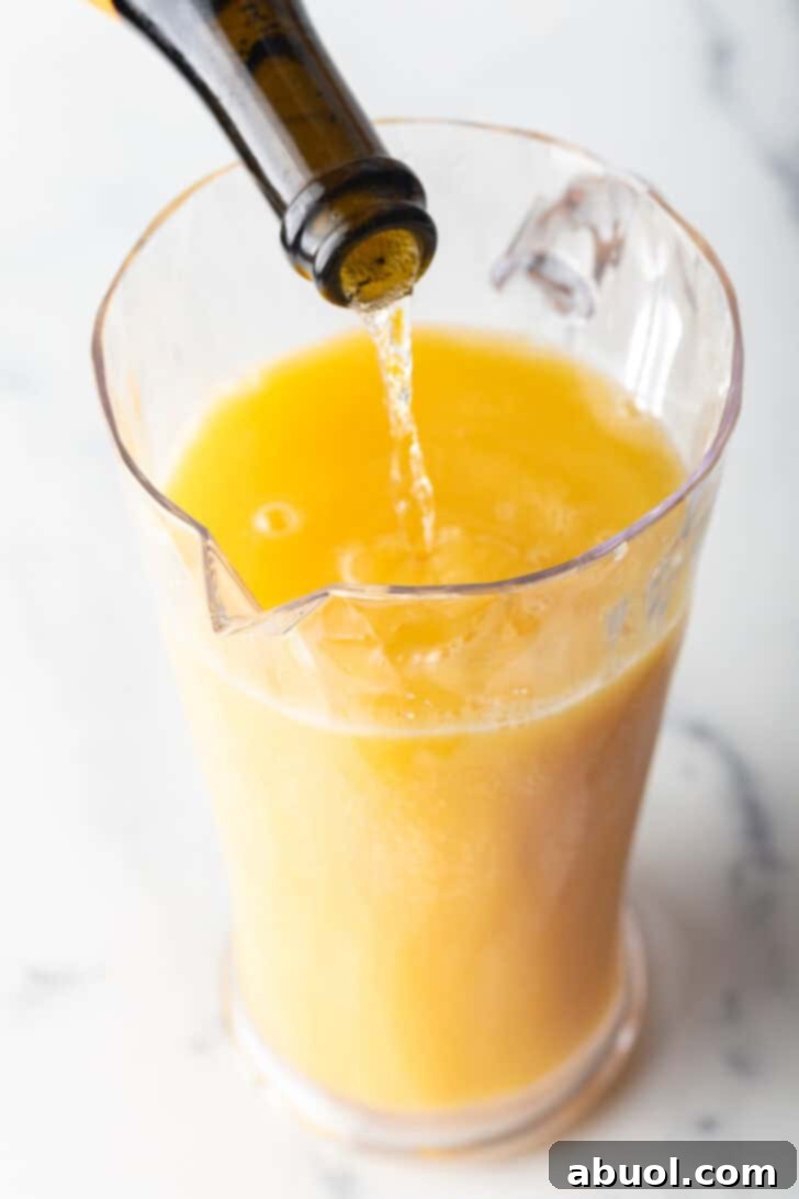 Pouring sparkling wine form the bottle into a glass pitcher with orange juice.