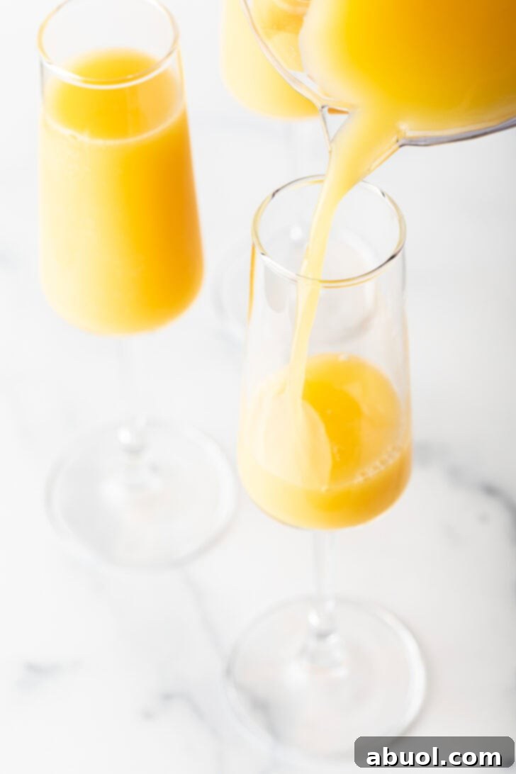 Pouring orange juice from a pitcher into a tall champagne glass.