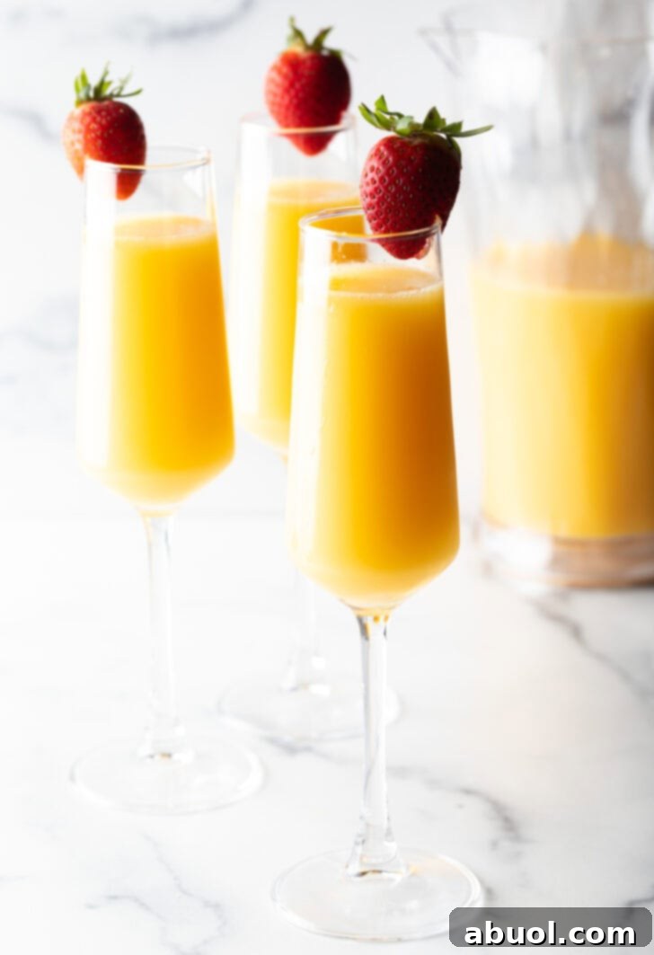 3 champagne glasses full of mimosa and each garnished with a whole strawberry on the rim.