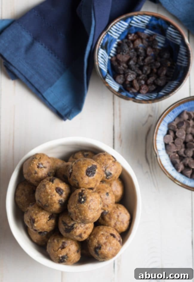 A top-down perspective of a white bowl overflowing with homemade oatmeal energy balls, featuring delightful specks of peanut butter, rich chocolate chips, and sweet raisins.