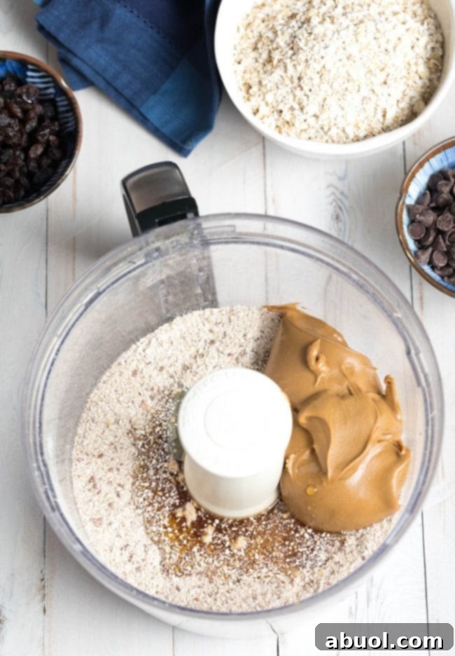 A generous scoop of creamy peanut butter being added to a food processor, ready to blend with other ingredients for the energy ball mixture.