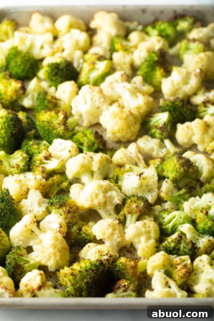 Broccoli and cauliflower florets, seasoned and coated in oil, spread in a single, even layer across a large baking sheet, ready for the oven.