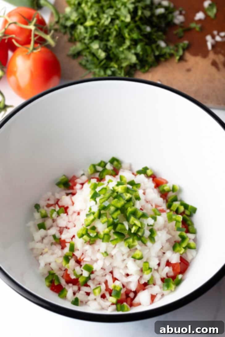 Chopped jalapenos and onion added to the bowl of chopped tomatoes, illustrating the mixing process.