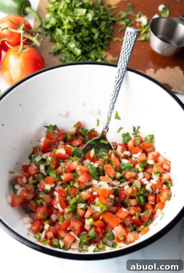 Combining the pico do gallo ingredients in a white mixing bowl with a spoon, ensuring even distribution.