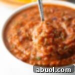 A metal spoon is showing a scoop of roasted salsa scooped from a white bowl.