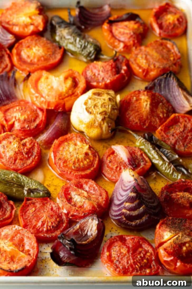 Top down view baking sheet brimming with roasted sliced tomatoes, jalapeno, and red onion chunks.