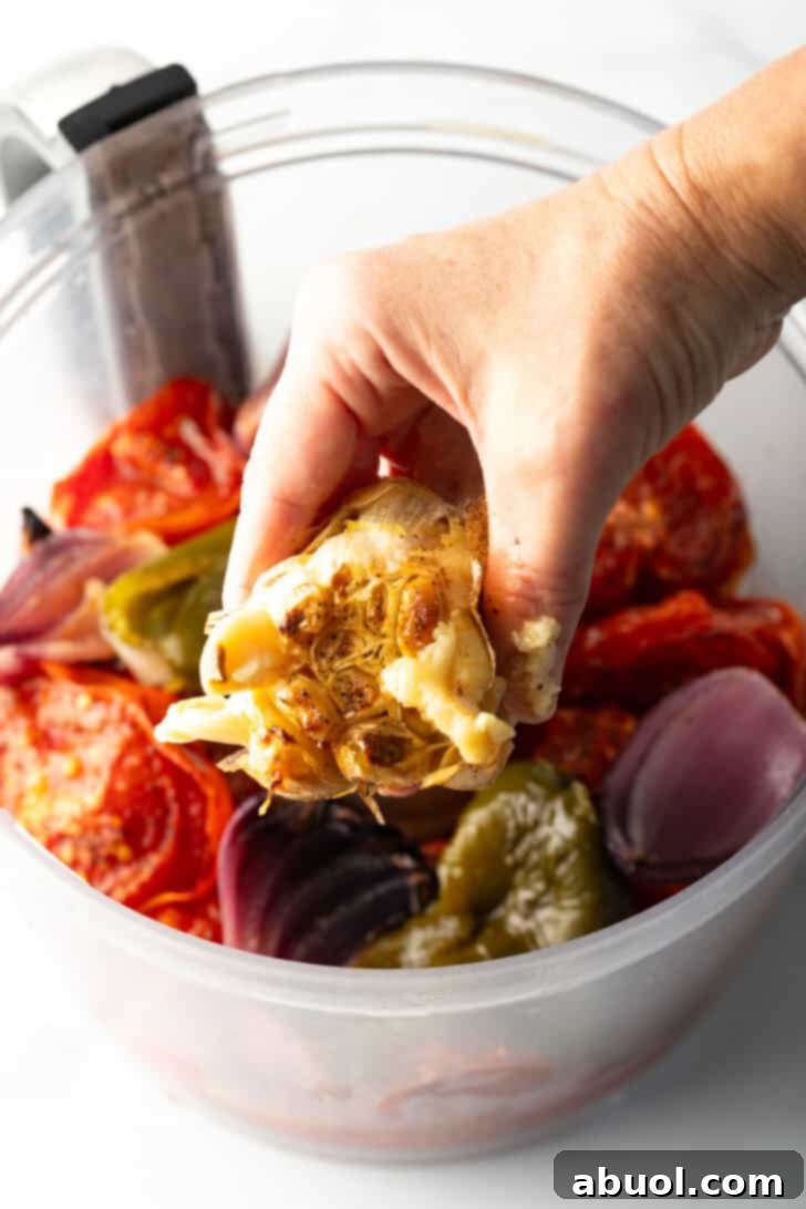 Hand squeezing roasted garlic into a food processor with other salsa ingredients.