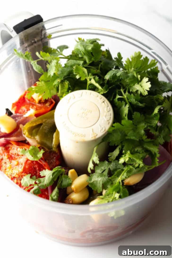 Food processor with fresh cilantro, tomatoes, jalapeno, and onion.