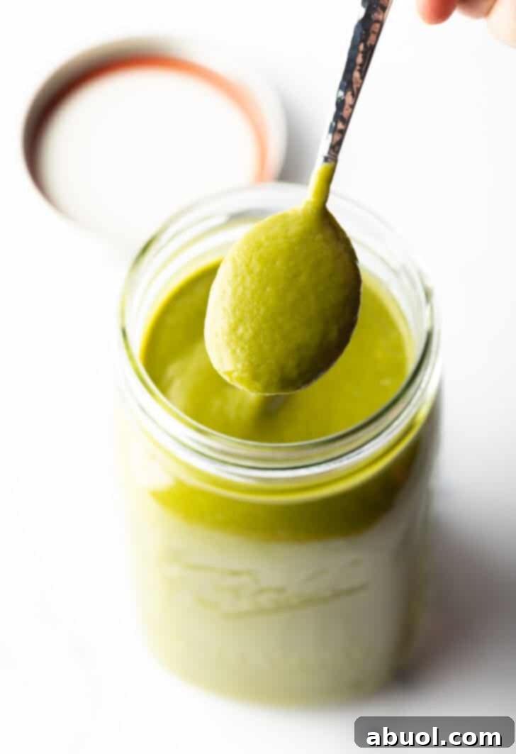 A spoonful of rich, green poblano sauce is lifted from a blender, showcasing its smooth texture.