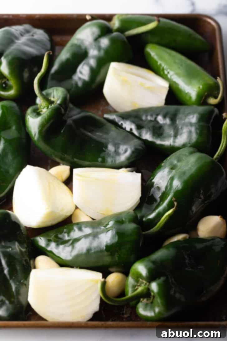 Poblano peppers, chunks of onion, and cloves of garlic arranged on a baking sheet before roasting.