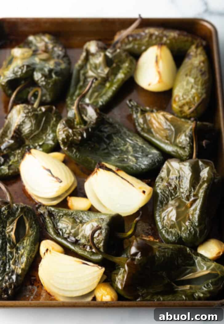 Roasted poblano peppers, softened onion chunks, and caramelized garlic cloves on a baking sheet after roasting.
