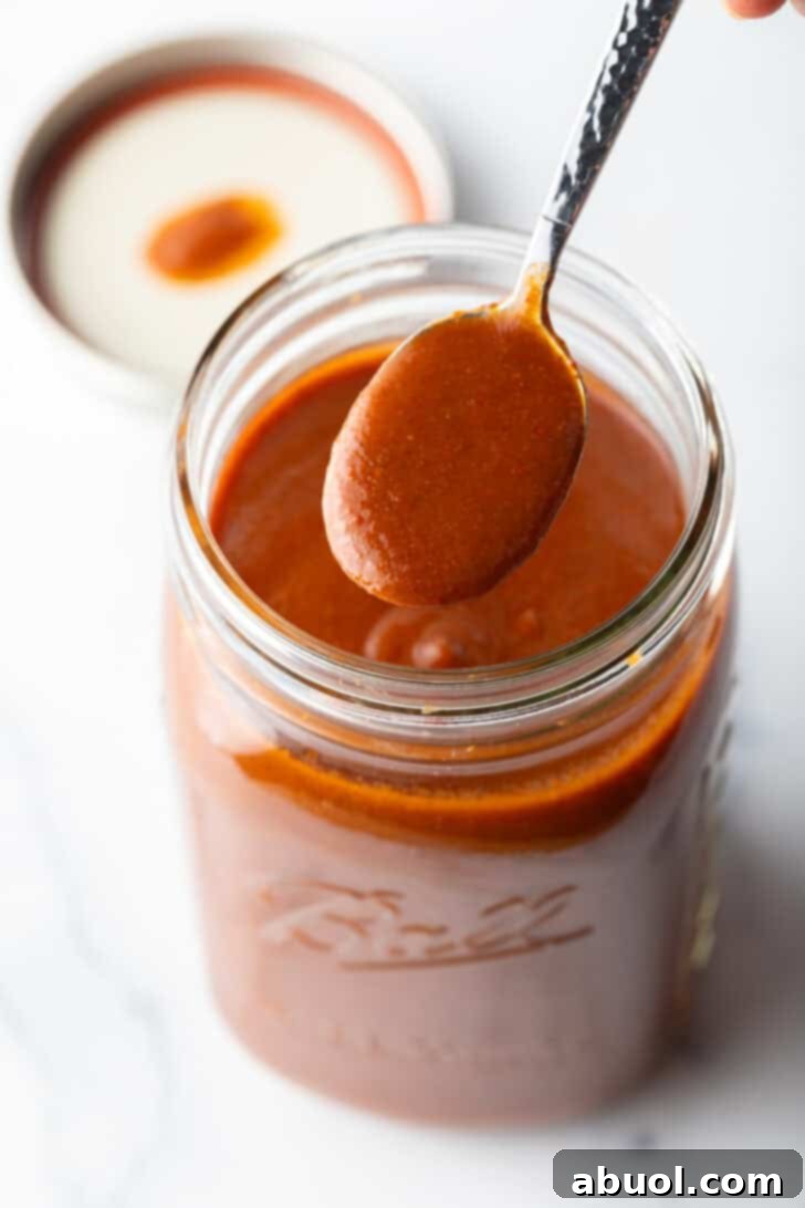 Spoonful of red enchilada sauce being held to camera over a large jar.