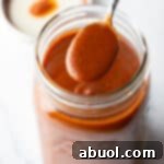 Spoonful of red enchilada sauce being held to camera over a large jar.