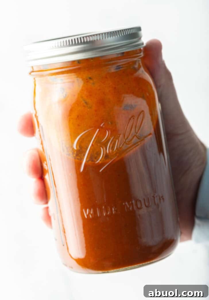 Hand holding a large glass mason jar filled with red enchilada sauce.