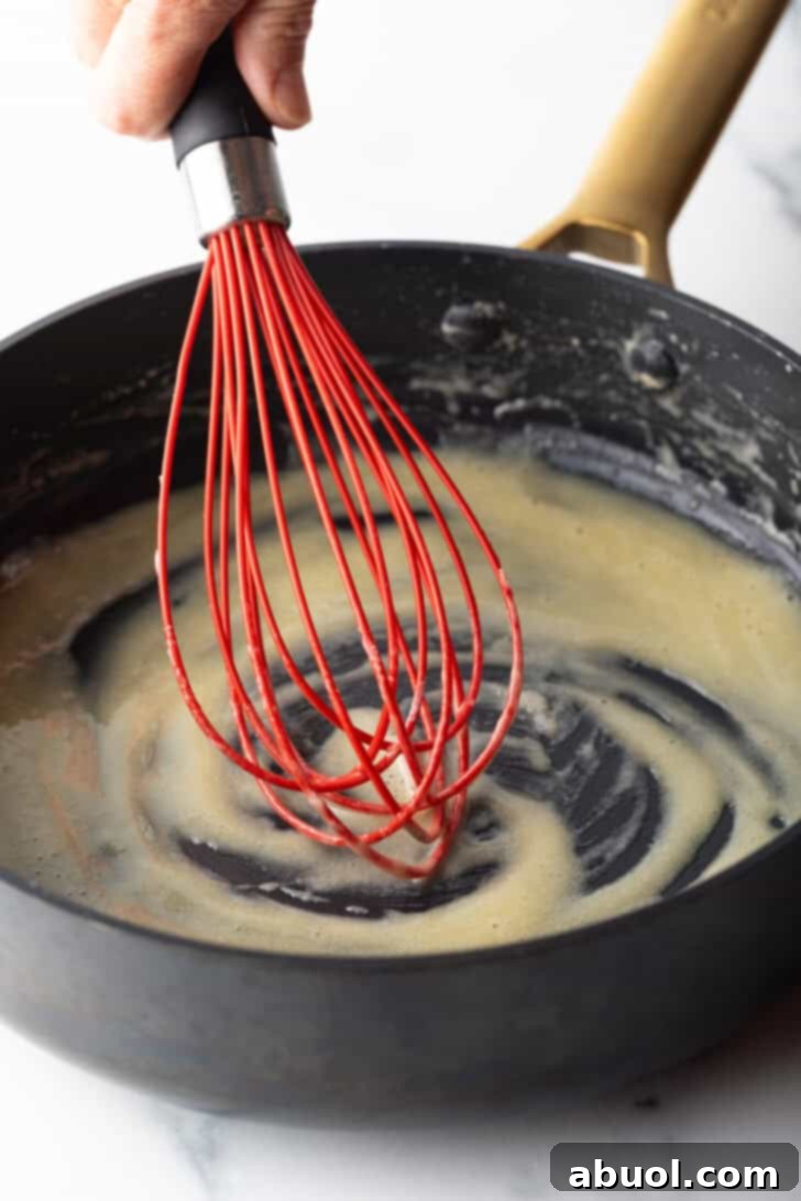Red whisk stirring butter in a black skillet.