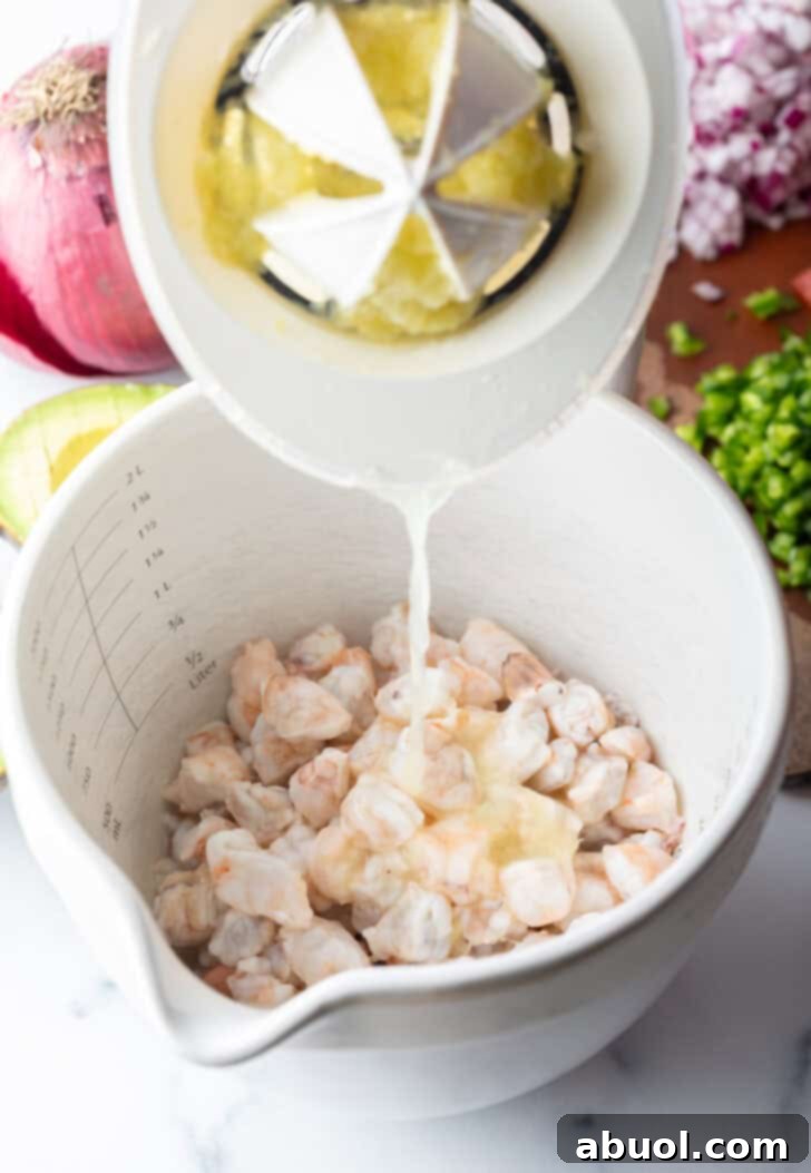 Pouring lime juice from a juicer into a white bowl of raw shrimp.