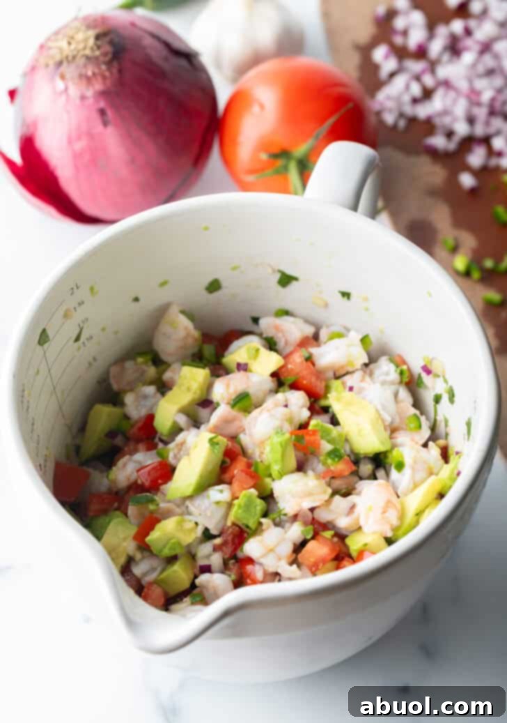 White bowl with a combination of shrimp, and chopped avocado, green and red peppers, and cilantro.