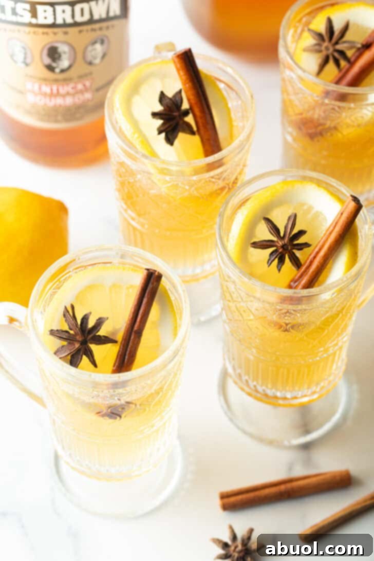 Crafting a Cozy Hot Toddy 4 3 glasses with yellow tea, garnished with a whole star anise and stick of cinnamon.