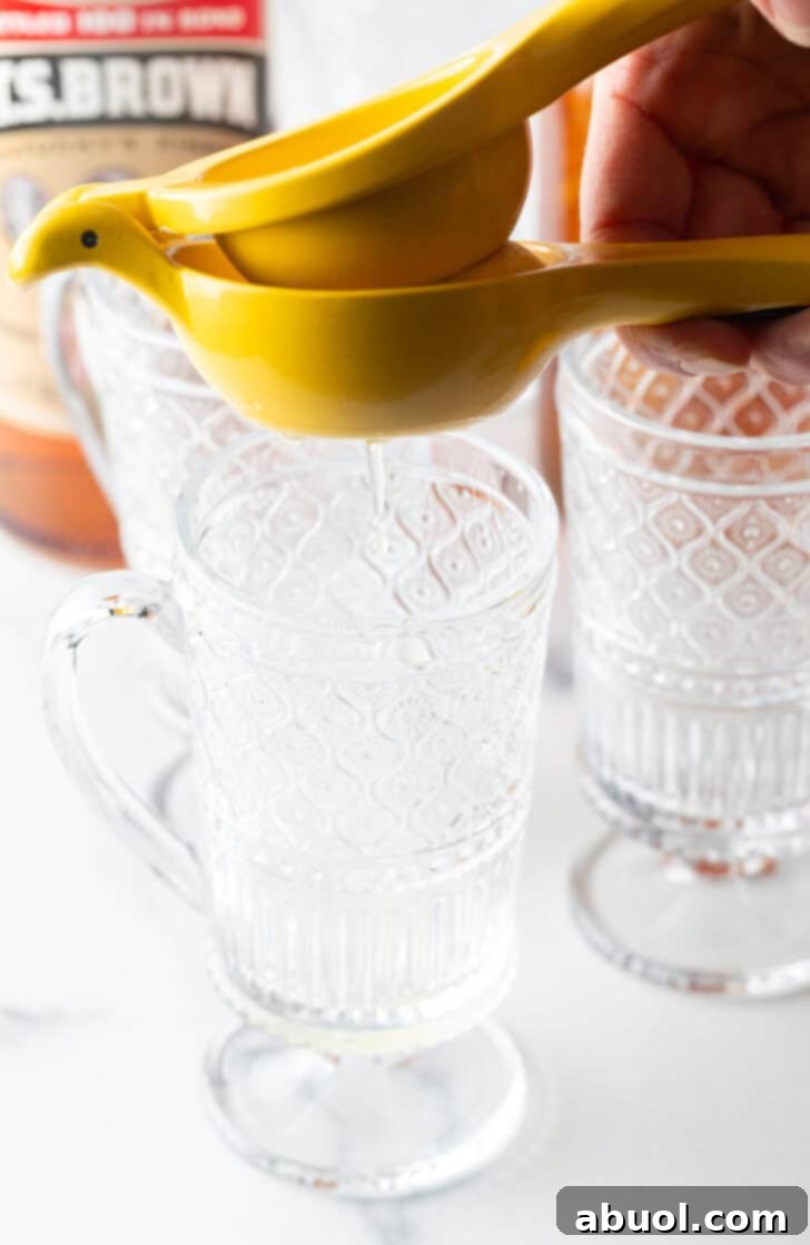 Crafting a Cozy Hot Toddy 6 Use a yellow juicer to juice a lemon over a clear mug with handle.