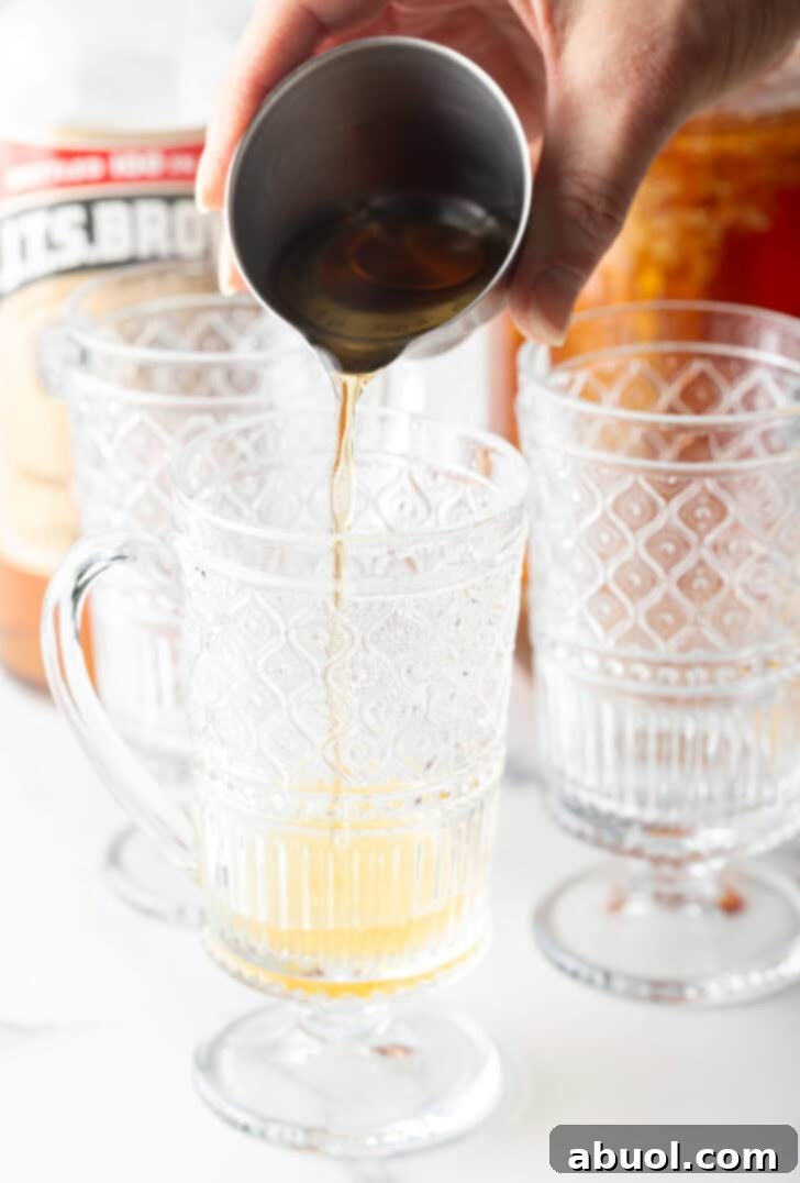Crafting a Cozy Hot Toddy 7 Add alcohol from a metal jig into a clear glass with a handle.
