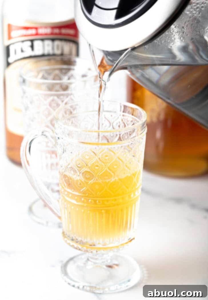 Crafting a Cozy Hot Toddy 9 Pouring tea from a metal kettle into a clear glass mug.
