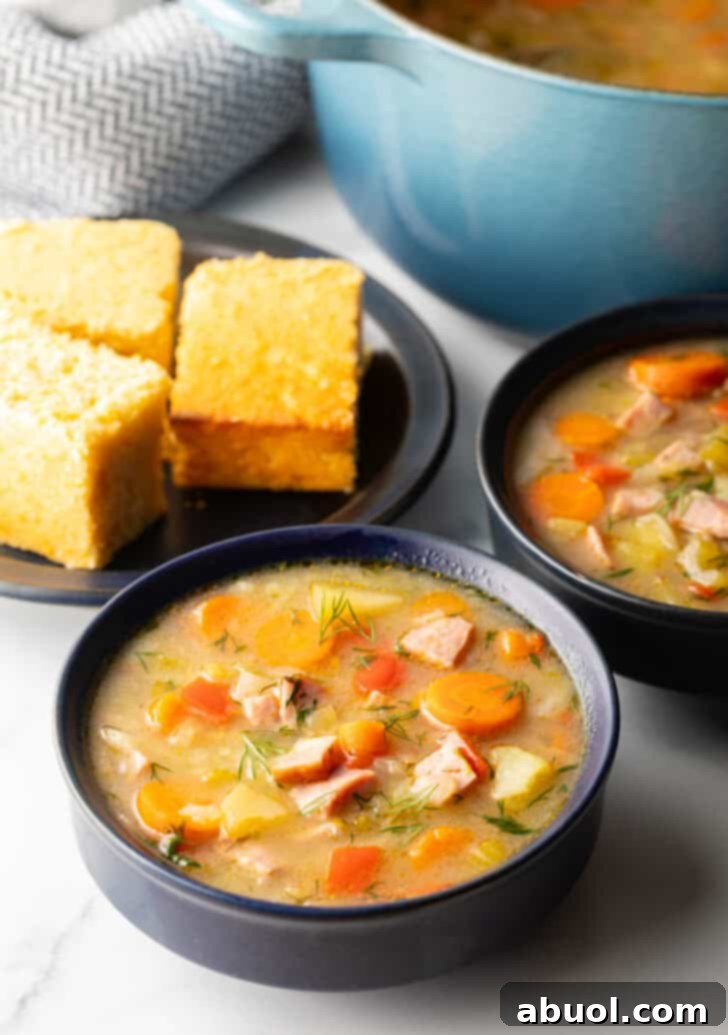 Two black bowls of ham and cabbage soup next to a black plate with 3 squares of cornbread, creating a warm and inviting scene.