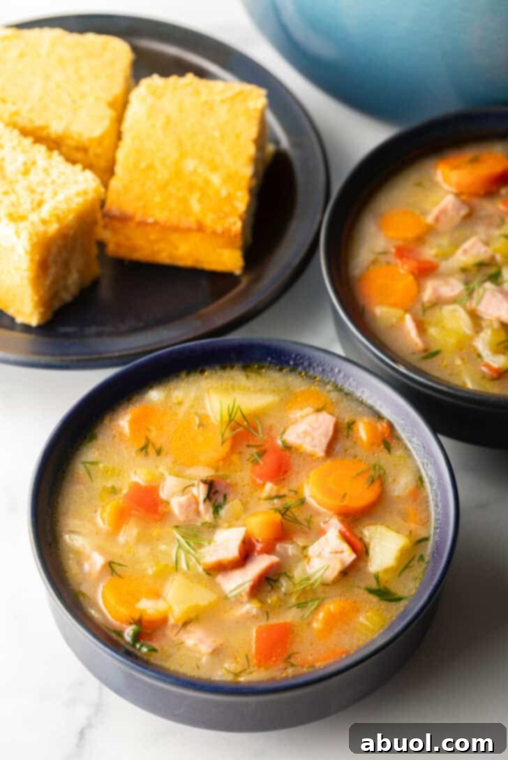 Two black bowls of ham and cabbage soup next to a black plate with 3 squares of cornbread, emphasizing a complete and satisfying meal.