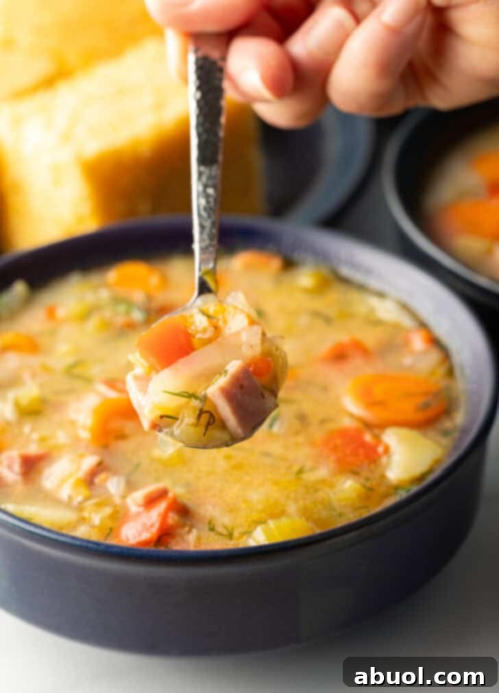 Spoonful of soup held over black bowl of cabbage and ham soup, showing to camera, highlighting its hearty texture.