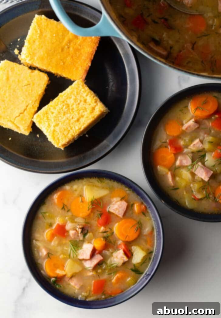 Top down view two black bowls of ham and cabbage soup next to a black plate with 3 squares of cornbread, showcasing the vibrant ingredients.