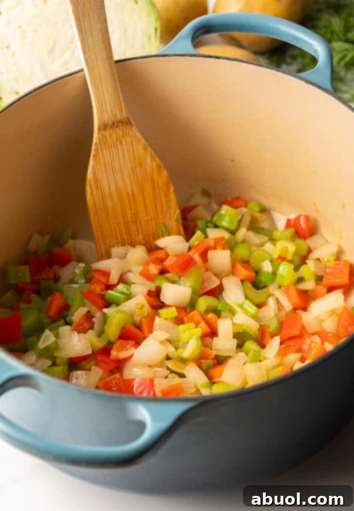 Cooking diced onion, carrots, bell pepper, and celery in a large blue cooking pot, creating a fragrant base for the soup.
