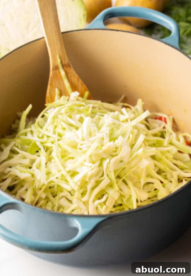 Large blue cooking pot with shredded cabbage, ready to be incorporated into the simmering broth, promising hearty texture.