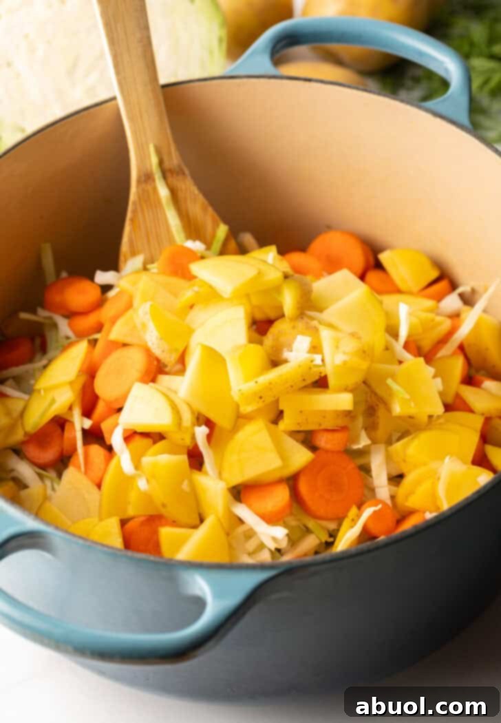Large blue cooking pot with chunks of potato, carrots, and cabbage, simmering gently to develop rich flavors and tender textures.