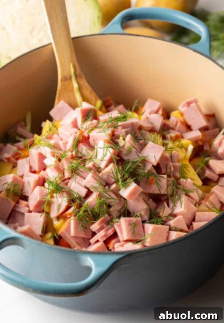 Large blue cooking pot with diced ham, vibrant vegetables, and fresh spices, nearing completion and ready to be served.