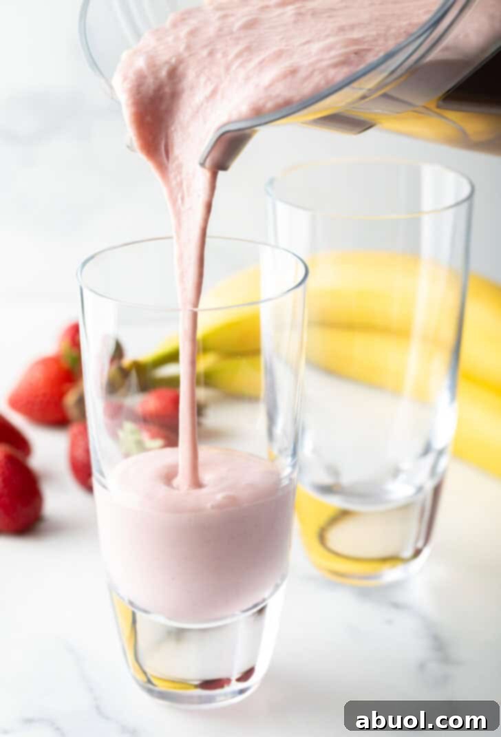 Pouring pink smoothie from a blender jar into a tall glass.