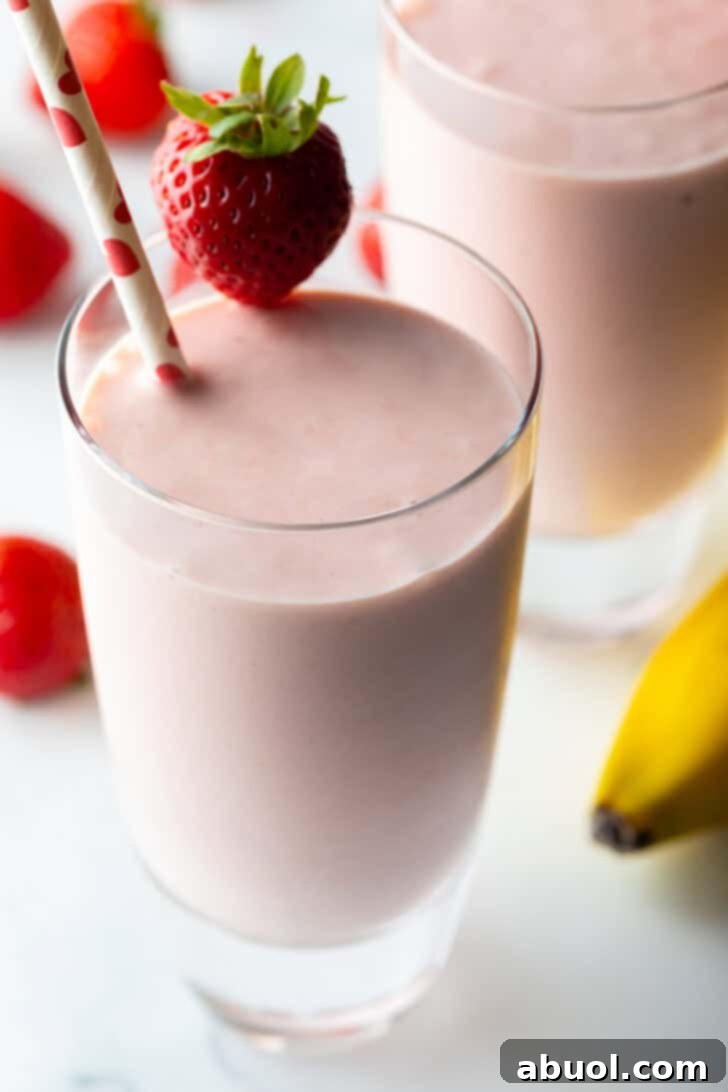Two tall glasses of strawberry banana smoothies, each garnished with a whole strawberry on the rim and a red and white straw.