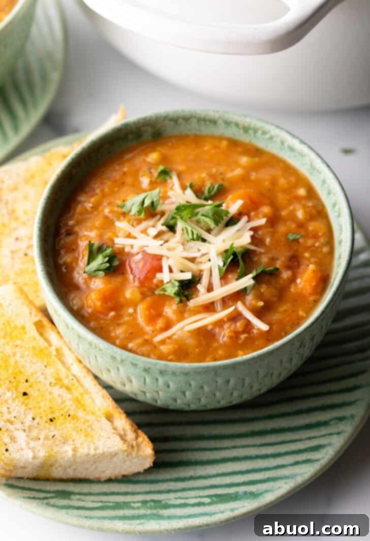 A vibrant green bowl of homemade red lentil soup, beautifully garnished with fresh chopped herbs and a sprinkle of shredded cheese. The bowl rests on a rustic plate, accompanied by two perfectly toasted baguette slices, inviting warmth and comfort.