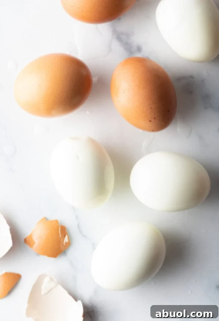 A top-down view showing four perfectly peeled hard-boiled eggs alongside three brown unpeeled eggs, demonstrating the successful outcome of the peeling techniques.