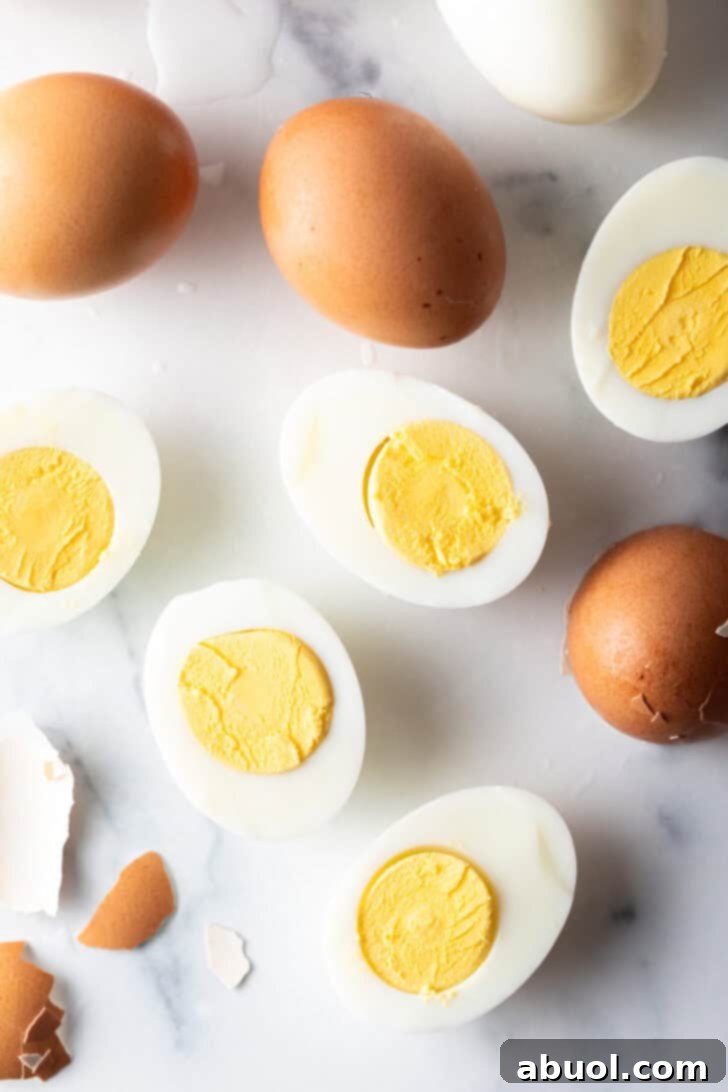 A comprehensive display of a dozen hard-boiled eggs on a white marble backdrop, including five egg halves, four brown eggs still in their shells, and one pristine white peeled egg, ready for any culinary use.