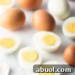 A dozen hard boiled eggs on a white marble backdrop. There are five egg halves, four brown eggs in the shell, and one white peeled egg.